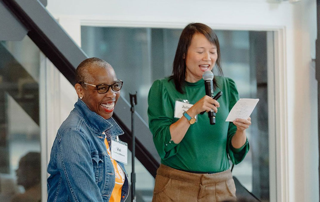 Thrive Two smiling members on a stage, one speaking into a microphone, reading from a card