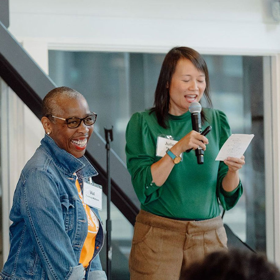 Presentation Two members on stage, one holding a microphone looking at a document